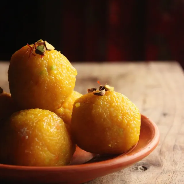 Boondi laddoo topped with saffron and pistachio on a clay plate