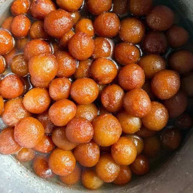 A pan full of small golden gulab jamun in syrup
