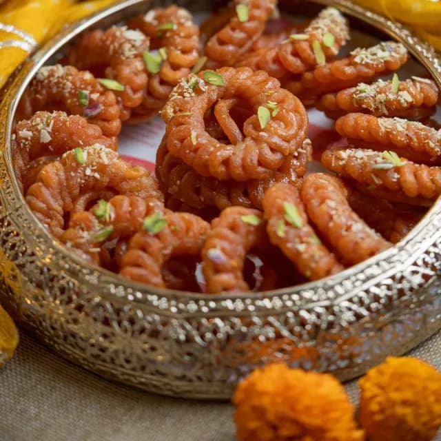 A brass bowl full of orange imarti
