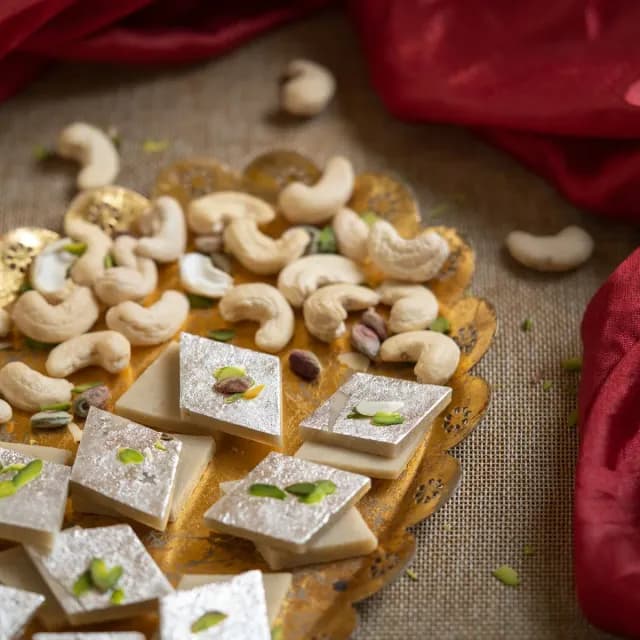 Diamond-cut kaju barfi with silver leaf beside cashews