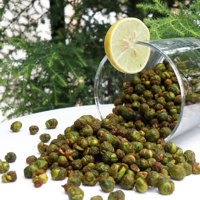 Crunchy masala green peas spilling from a glass, with a slice of lime