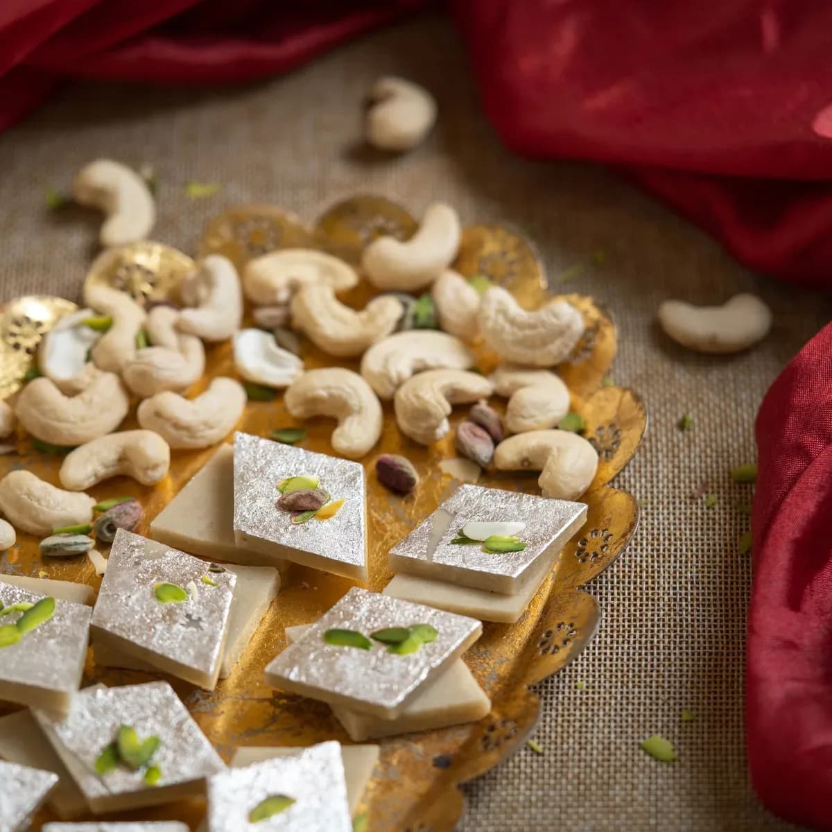 Diamond-cut kaju barfi with silver leaf beside cashews